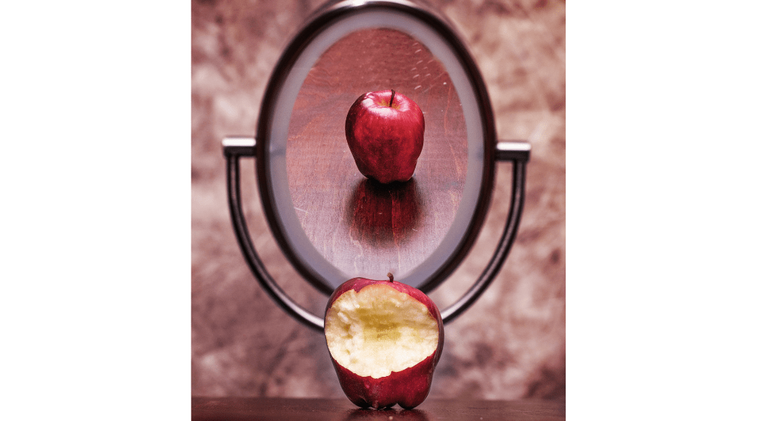 a half eaten red apple reflecting in a mirror, so the mirrored perspective shows a pristine apple