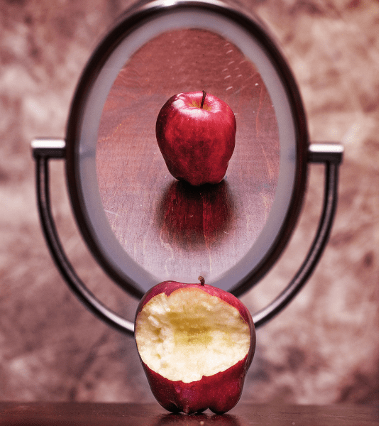 Untitled design (5) a half eaten red apple reflecting in a mirror, so the mirrored perspective shows a pristine apple
